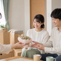 友人が新居で新婚のふたりへ小さな入籍祝いの花を手渡すイメージ
