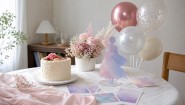自宅のテーブルにケーキ、アクリルスタンド、ピンクの花を飾った本人不在の誕生日会のイメージ