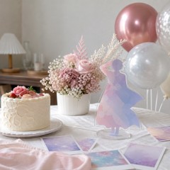 自宅のテーブルにケーキ、アクリルスタンド、ピンクの花を飾った本人不在の誕生日会のイメージ